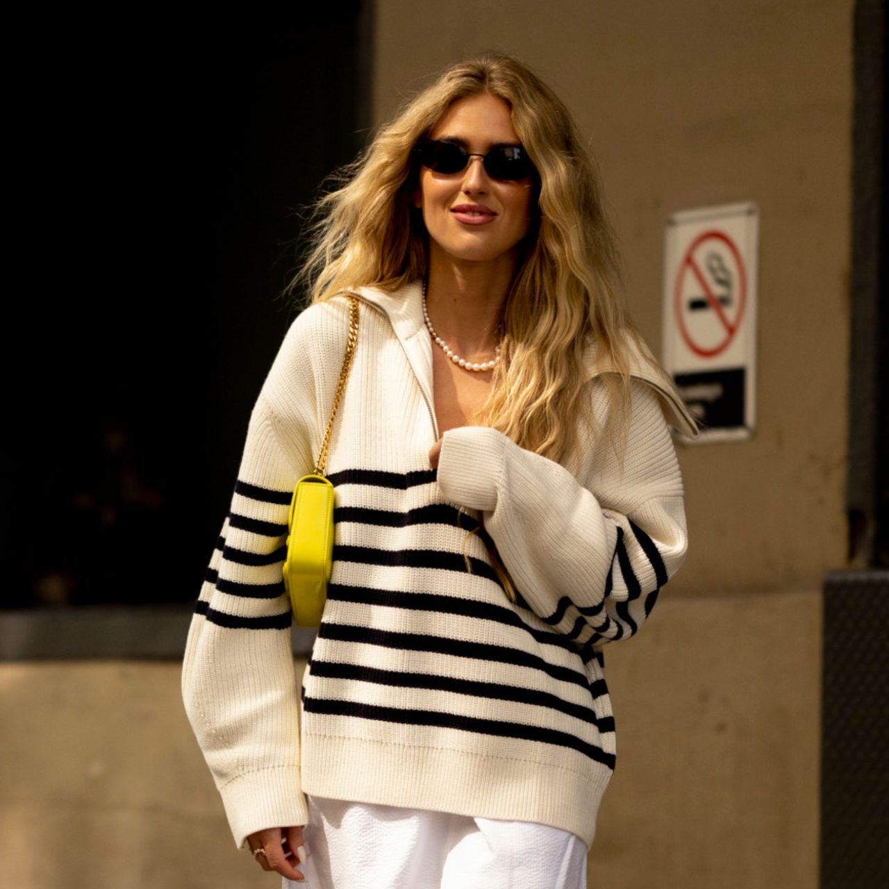 woman wearing striped sweater, white pants, yellow bag, and sunglasses