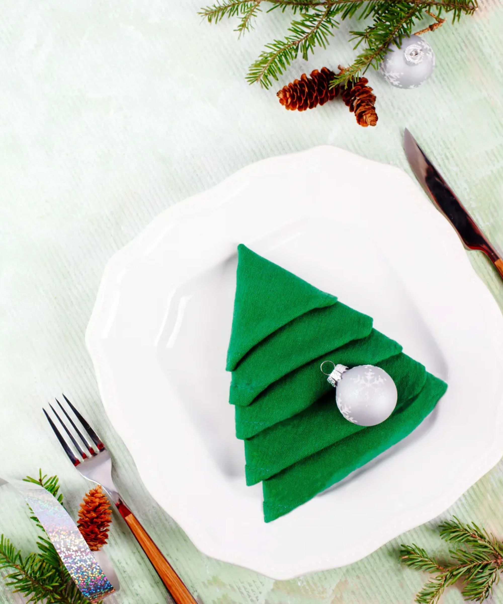 Green napkin folded into Christmas tree shape, with silver tree ornament on top