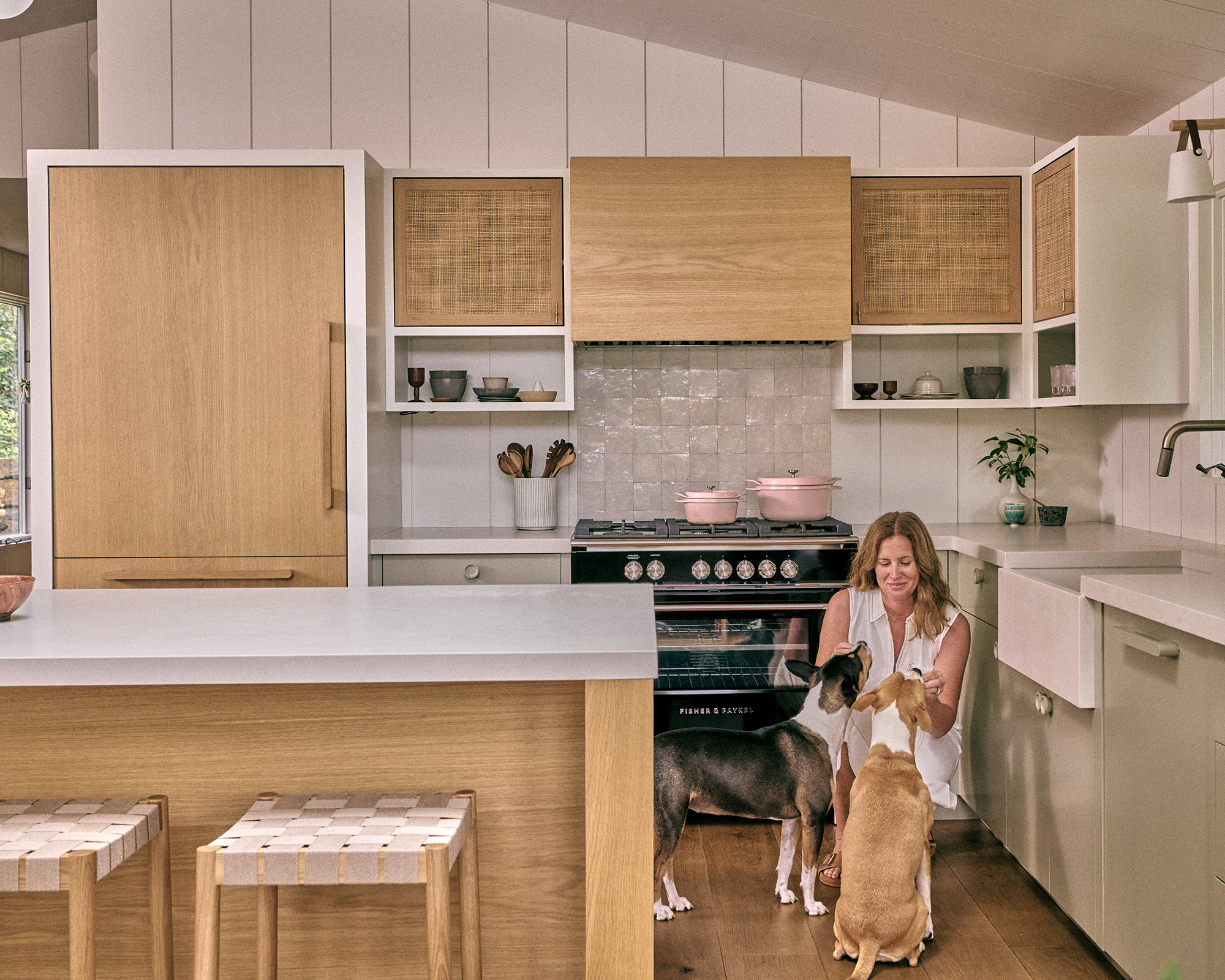 wood kitchen with white tiles and jess cooney crouching down petting two dogs