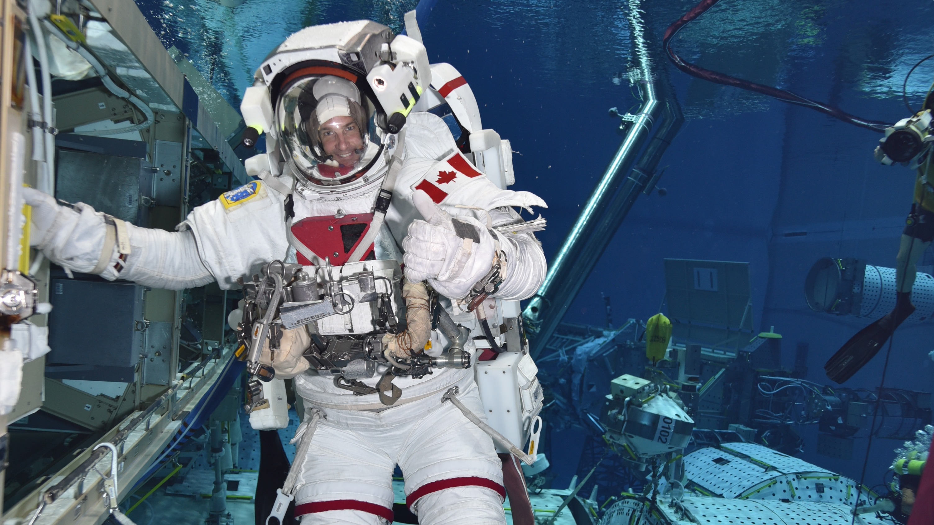 Jeremy Hansen en un traje espacial submarino.  Sostiene el casco con su mano derecha.  La bandera canadiense es visible en su hombro.