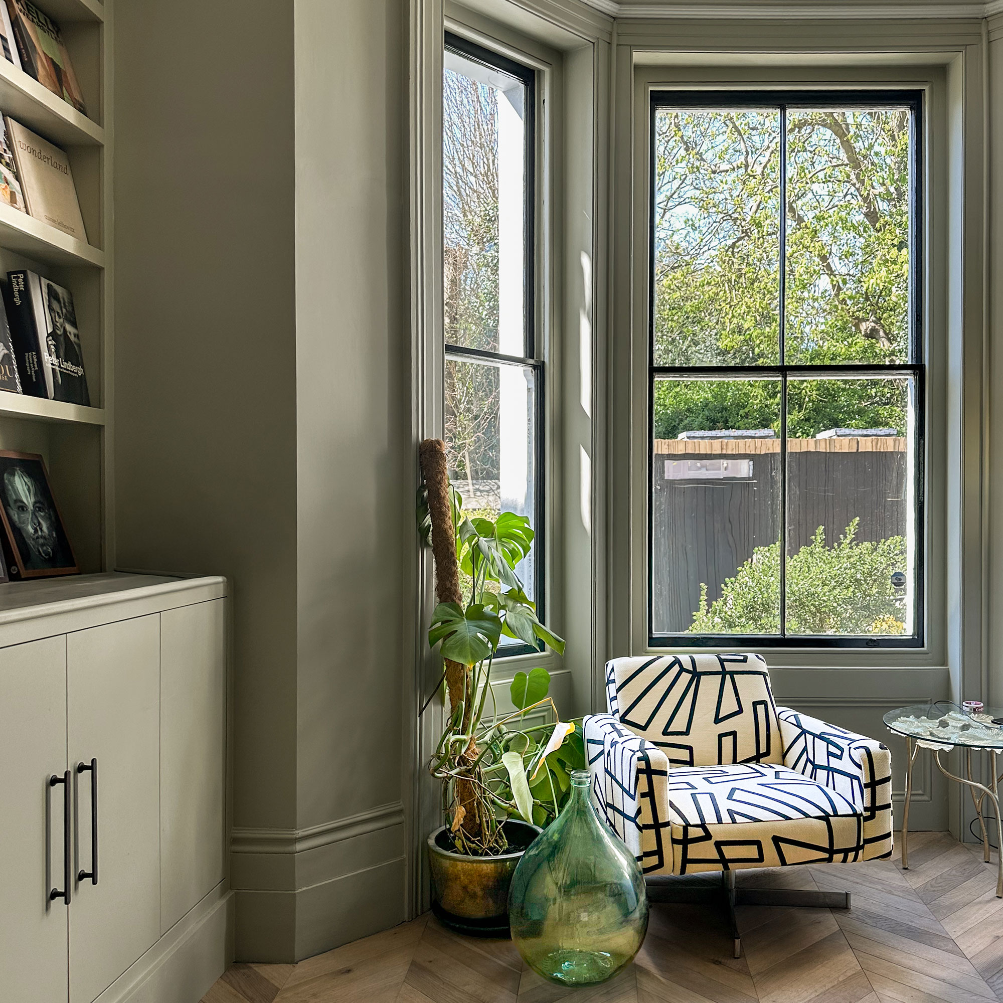 Abstract printed armchair sitting beside houseplant and oversized glass vase in by window area