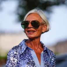 best serums for mature skin - Grece Ghanem wears brown sunglasses, gold earrings, purple sequin shirt