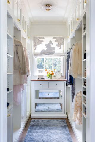 Dressing room with built-in mirrored drawers and fitted shelves and hanging space with pink blouses hanging up