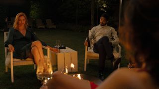Evie and Pete sit across from Becka in evening wear at their barbecue from The Couple Next Door episode 1.