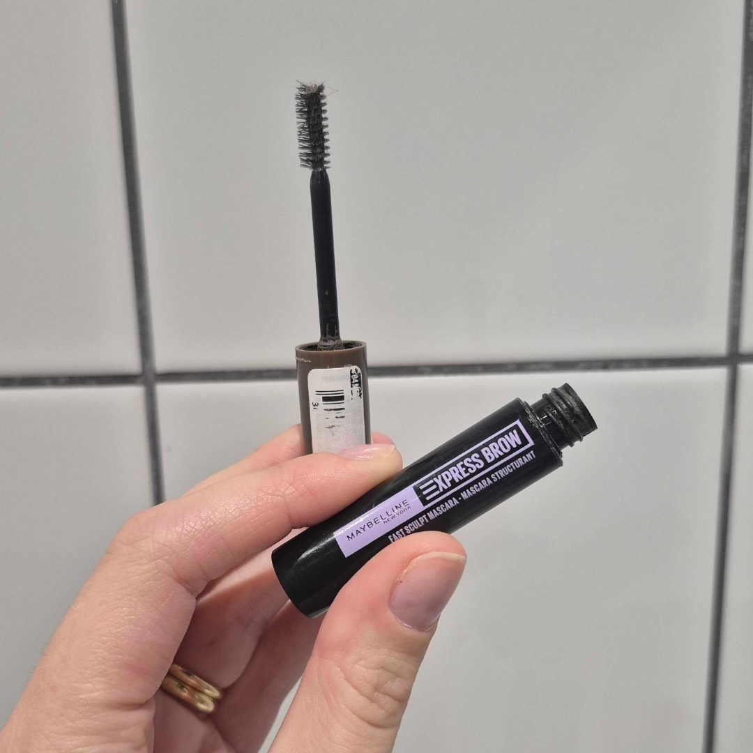 Hand holding empty tube of Maybelline Express Brow Fast Sculpt Eyebrow Mascara