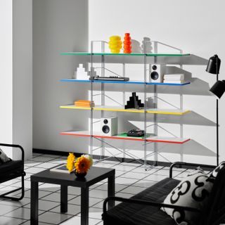 A white living room with black and white flooring. There is a black loveseat, black coffee table, and black accent chair in view. The shelving on the back wall is modern and each shelf a different color.