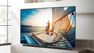 The Samsung QN90C TV on a white TV bench, showing footage of a man sailing on the screen
