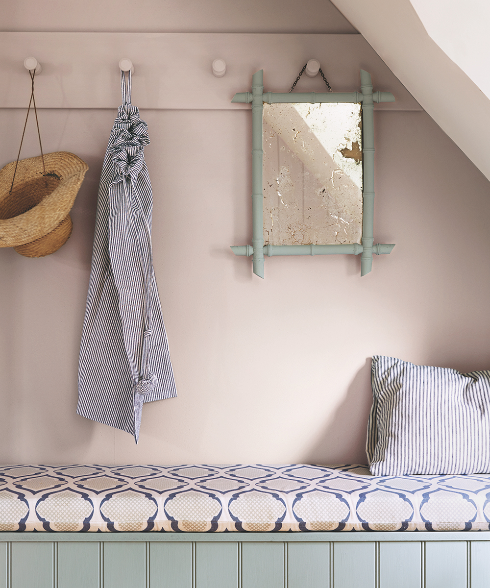 A pink wall with peg rail and banquette beneath