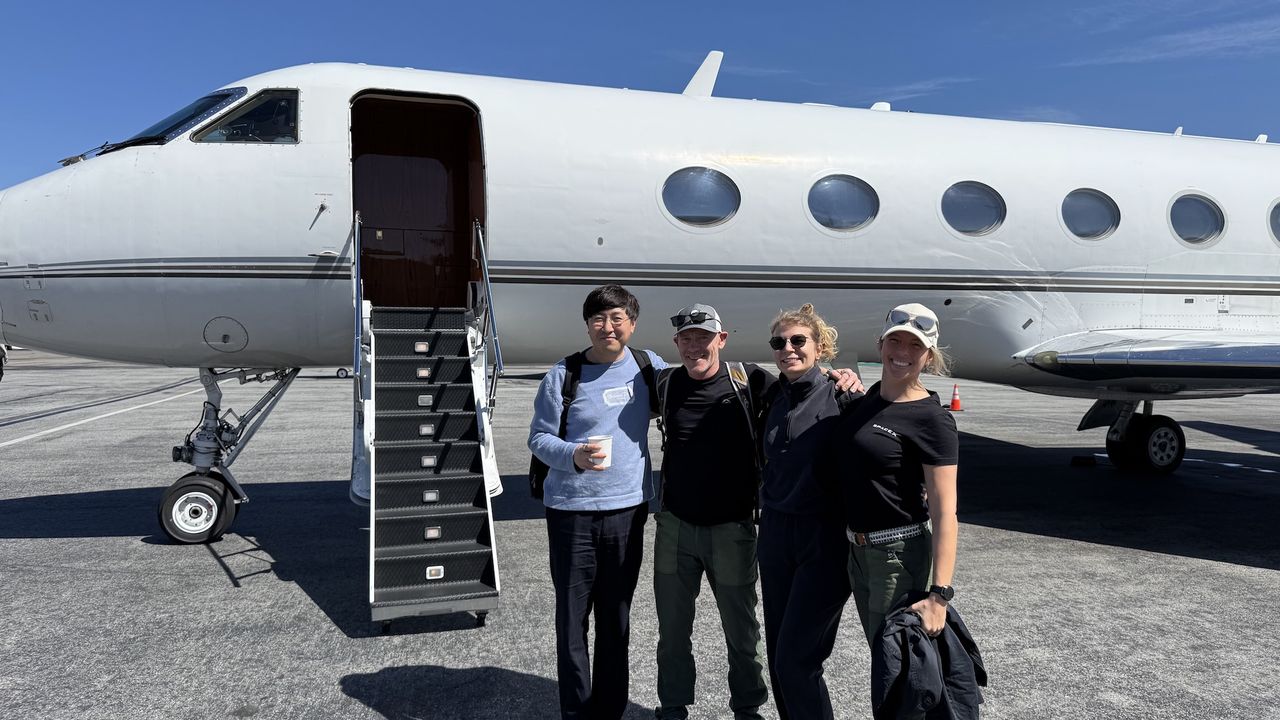 four humans stand next to an airplane