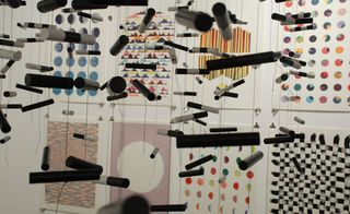 Foreground: Black and White Swarm, 2009. Many microphones hanging from the roof in front of a wall with paintings on.