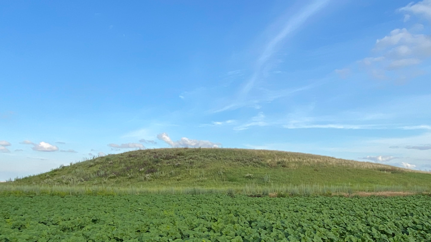 a grass-covered mound rises up against a blue sky