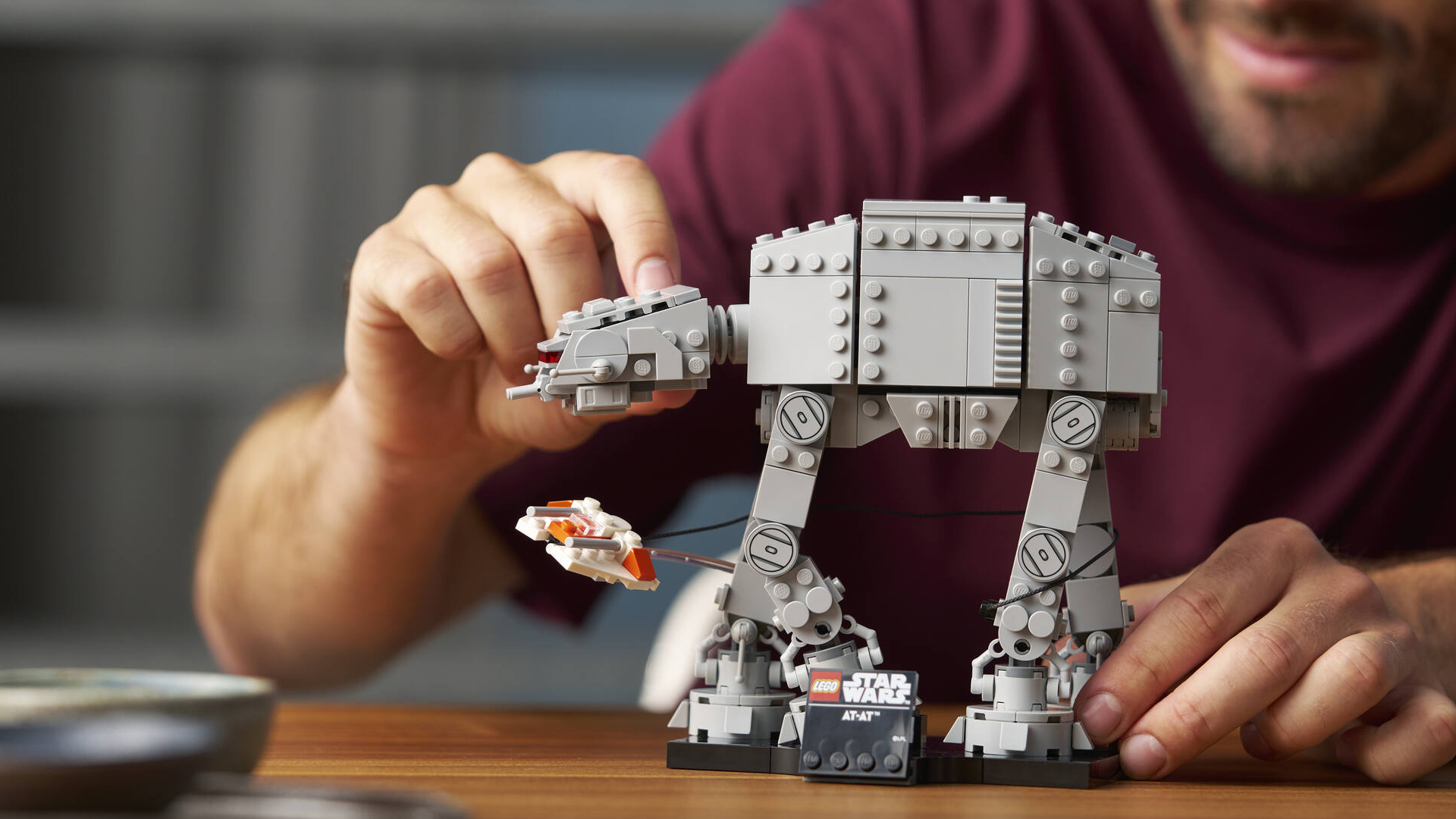 A man poses a Lego AT-AT's head while sat at a table