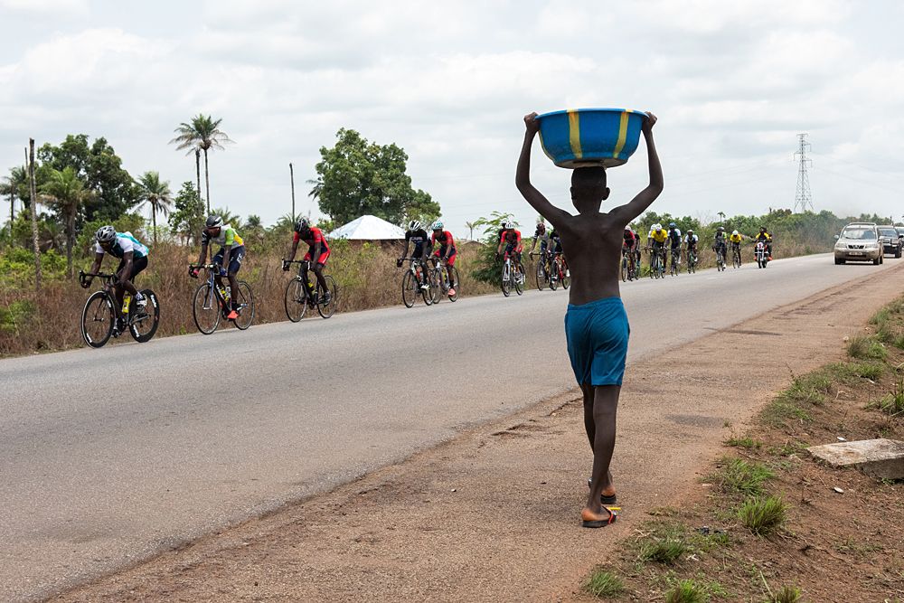 The peloton hurtles past a pedestrian on the road to Lunsar from Freetown