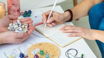 person writing in a notebook, with crystal and stones surround them on a desk