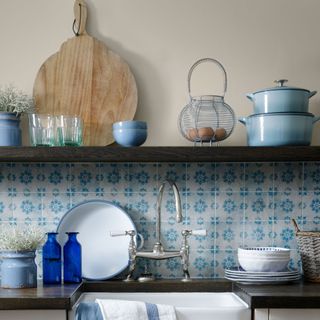 blue and white kitchen wall tiles under single dark wood shelf displaying light blue casserole pots