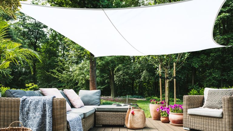 a white shade sail over a corner sofa with outdoor rug and potted flowers