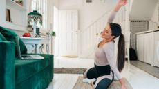 Woman performing Pilates on a living floor, sitting in front of a laptop resting on a couch