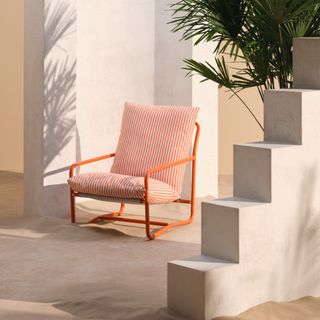 John Lewis Marcy Sling Garden Chair in burnt orange set in sand with a palm in the background