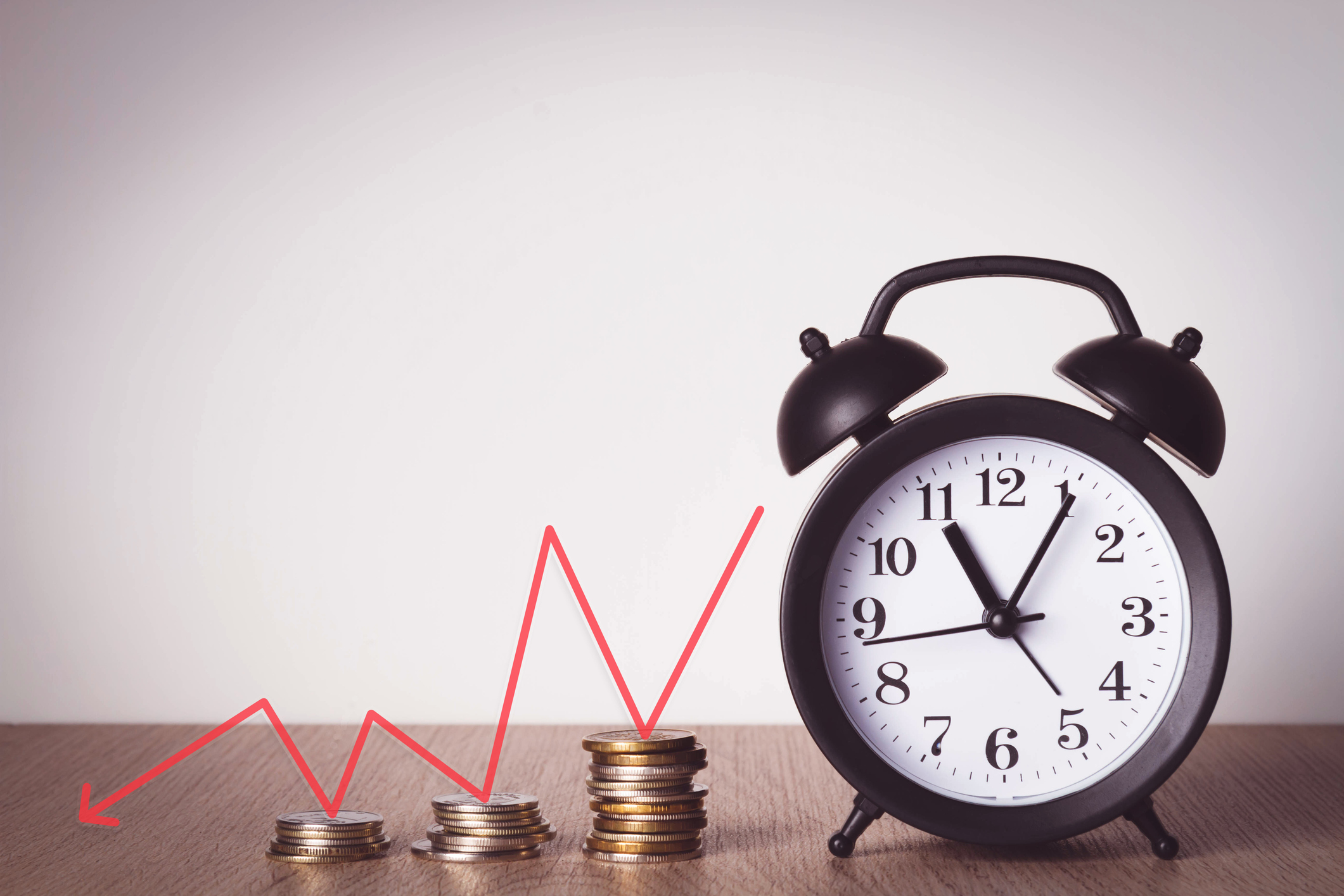 An alarm clock next to stacks of coins.