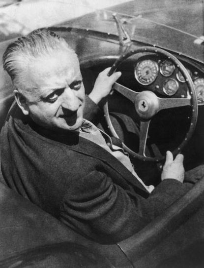 Enzo Ferrari sits behind the wheel of one of his famous cars.