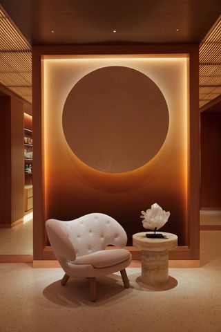 A golden-glowing modernly designed spa features whimsical furnishings including a white shearling armchair and a sun-like wall installation.