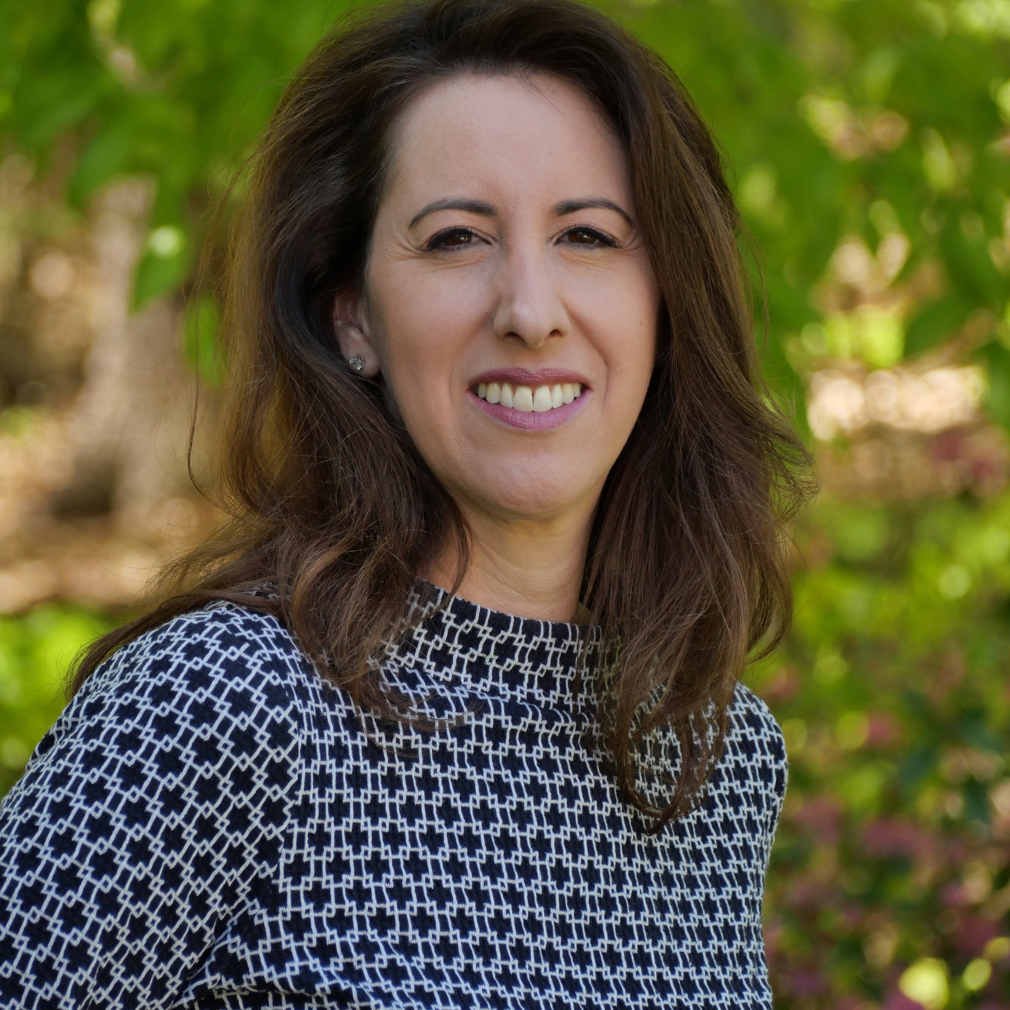 Lauren Saltman, professional organizer and founder of Living. Simplified, a woman with dark hair wearing a black and white patterned blouse pictured against a blurred garden background