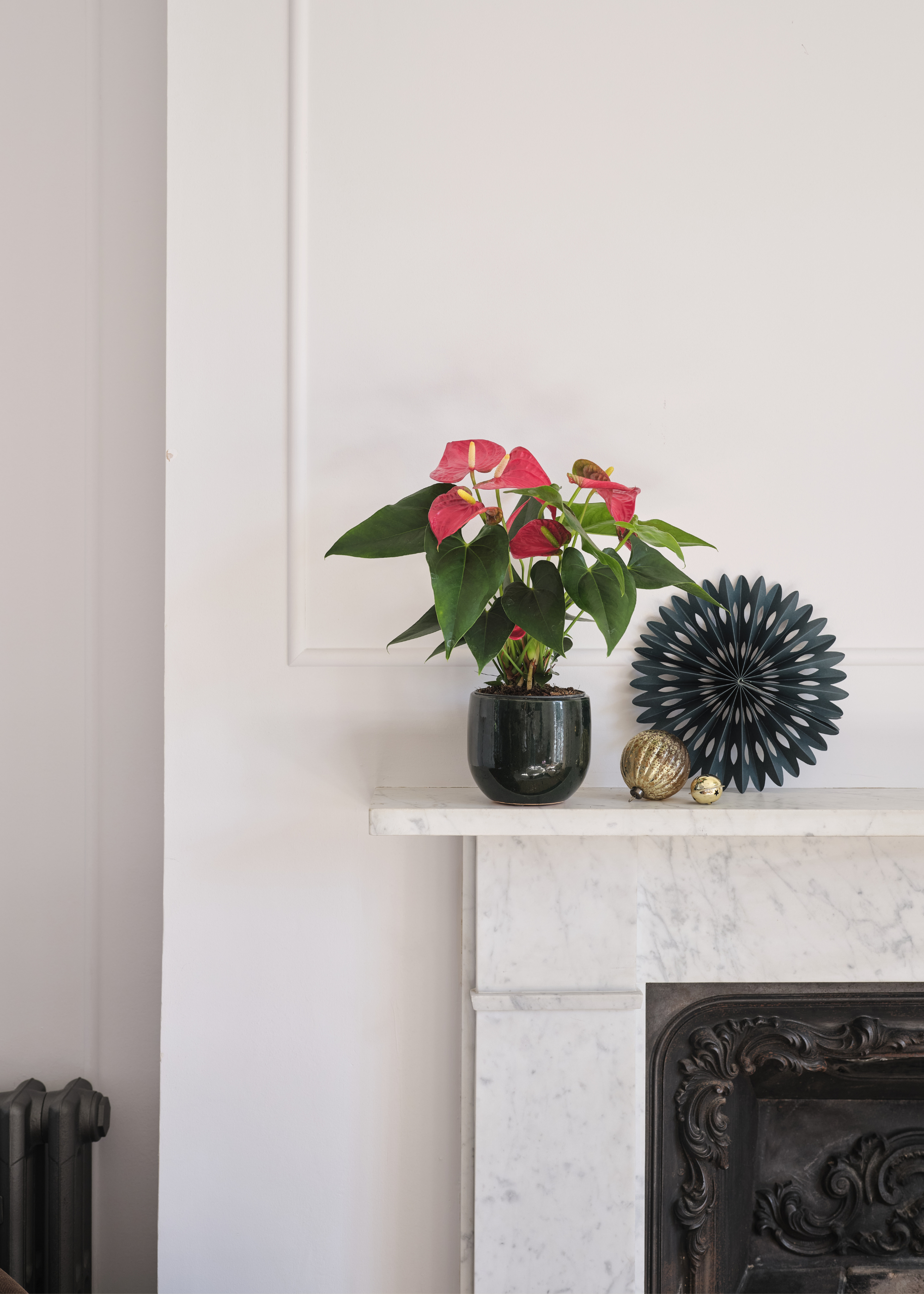 A potted anthurium on a marble mantel by a paper ornament