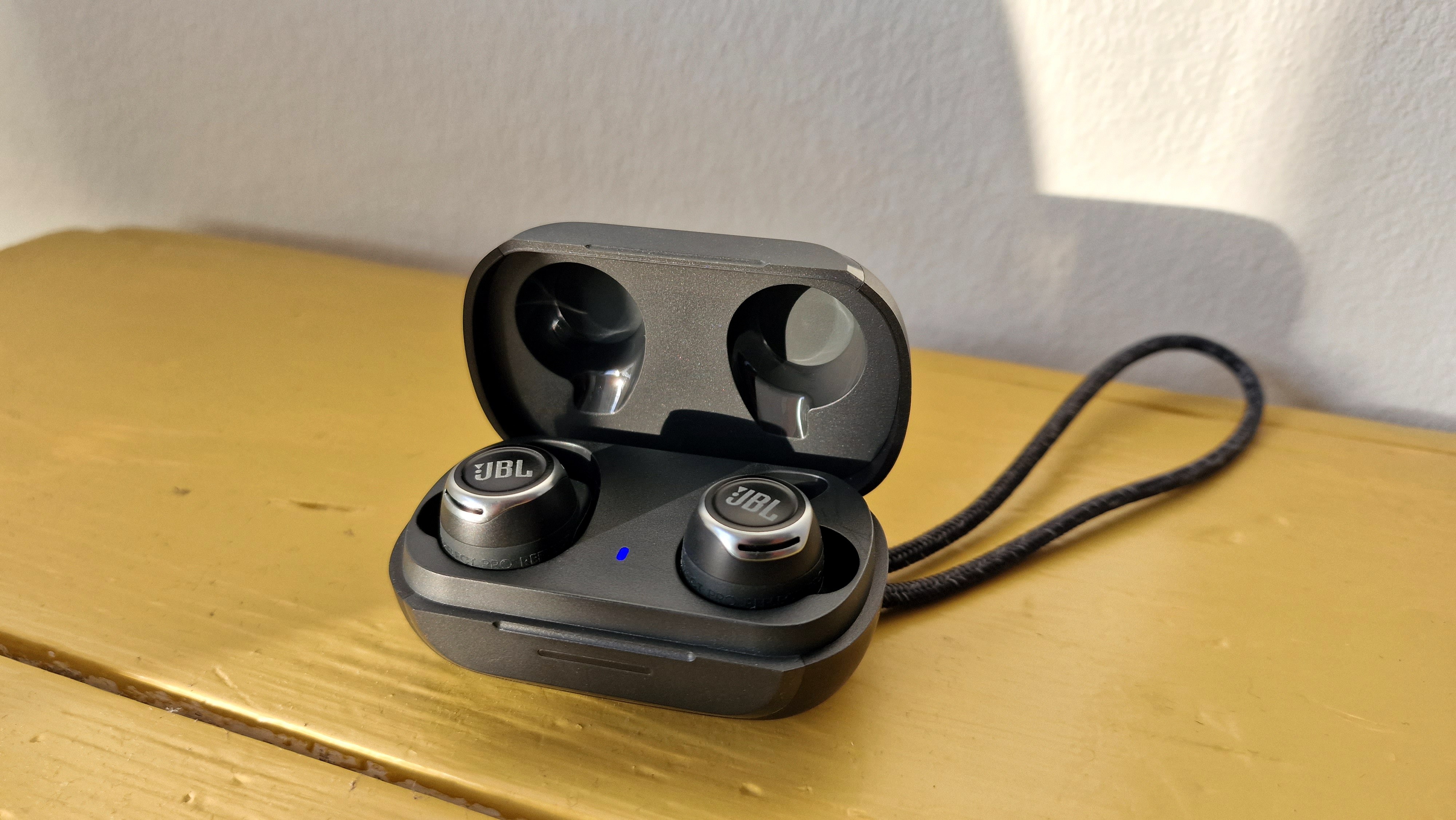 JBL Reflect Flow Pro høretelefonerne ligger i etuiet, der står på en gul hylde