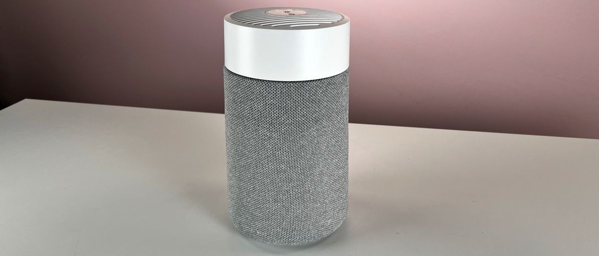 The white and gray Blueair Blue Pure Mini Max sits on a pale surface in front of a pink background.