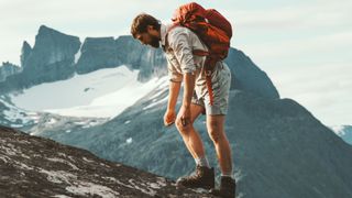 A tired hiker stoops over as he hikes up a mountain with a backpack on