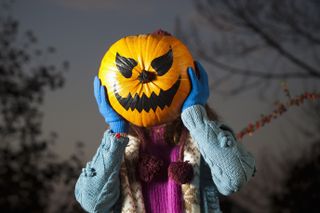 Woman holding jack o lantern over face on Halloween