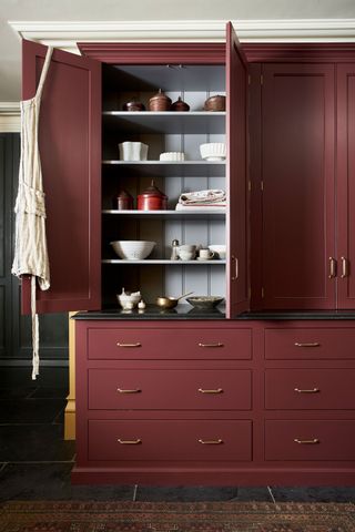 Freestanding shaker style kitchen larder cupboard painted in deep red against mustard yellow walls