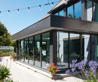 The exterior of a glass extension on a sunny day next to a bright patio