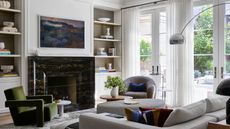 modern living room with white walls, gray sofa, dark green armchair and black fireplace