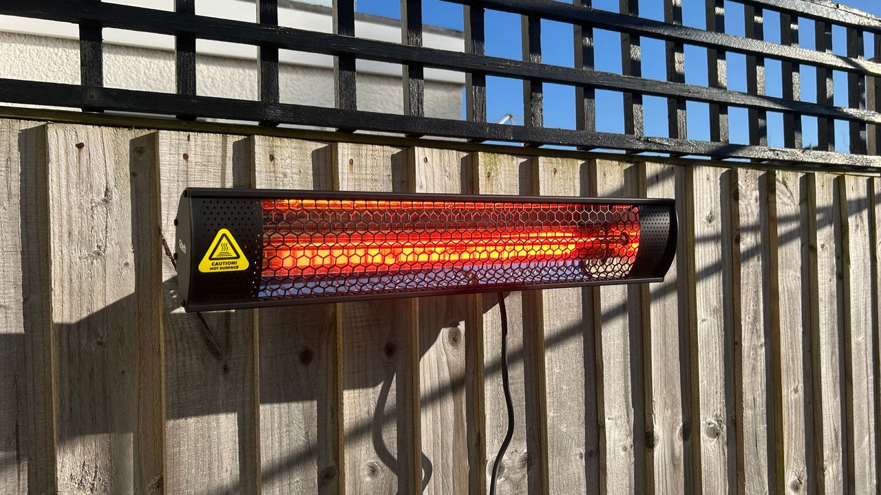 Gtech HeatWave Patio Heater on wooden fence in garden, powered on