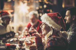 A happy woman enjoying Christmas drinks with several others round a Christmassy table.