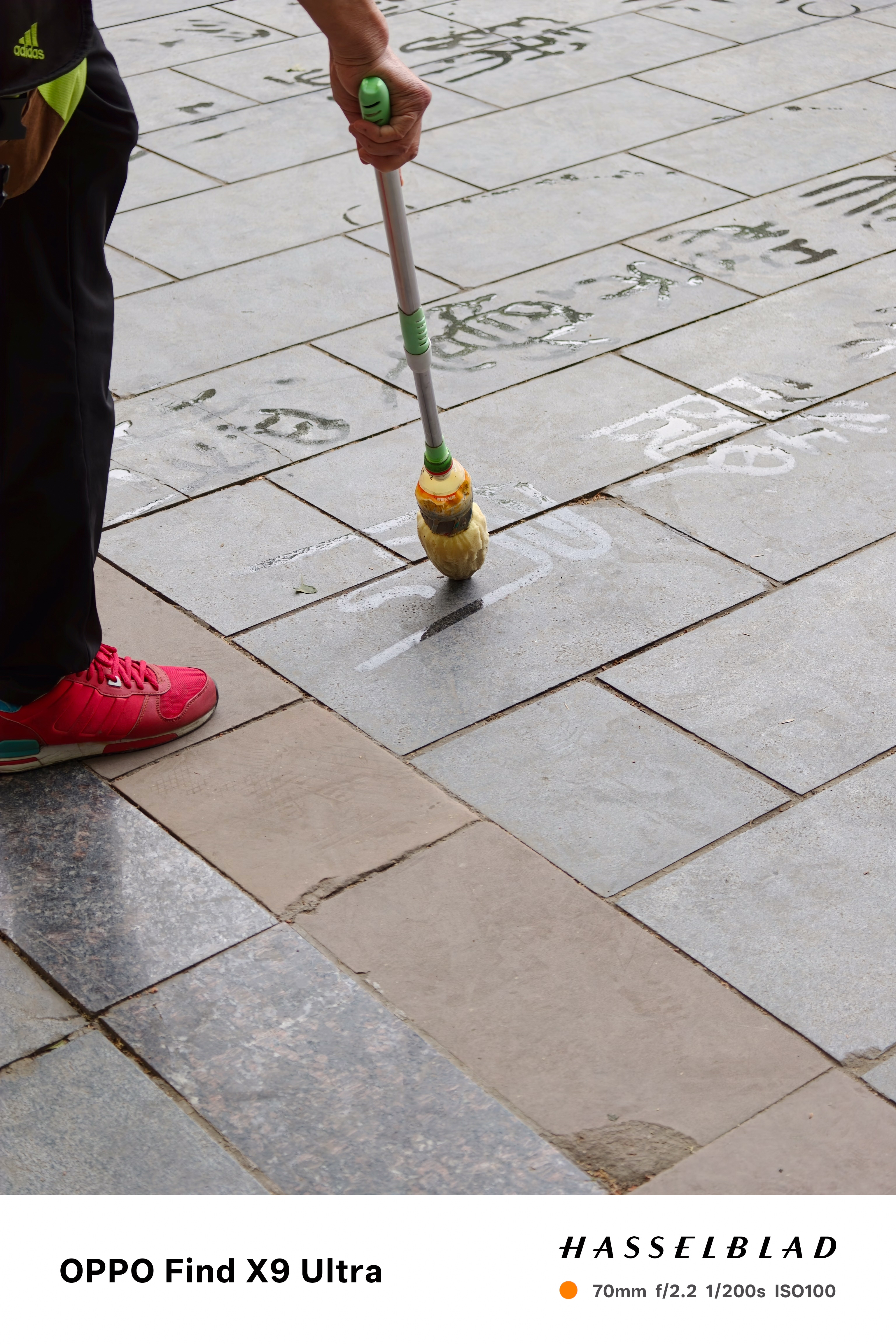 Person using a long-handled brush to write water calligraphy on paving stones