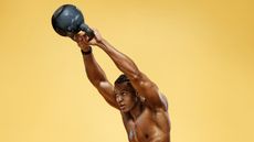 Muscular man performing kettlebell swings against yellow background