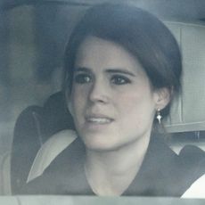 Princess Eugenie wearing a black coat and dangling earrings sitting in a car 