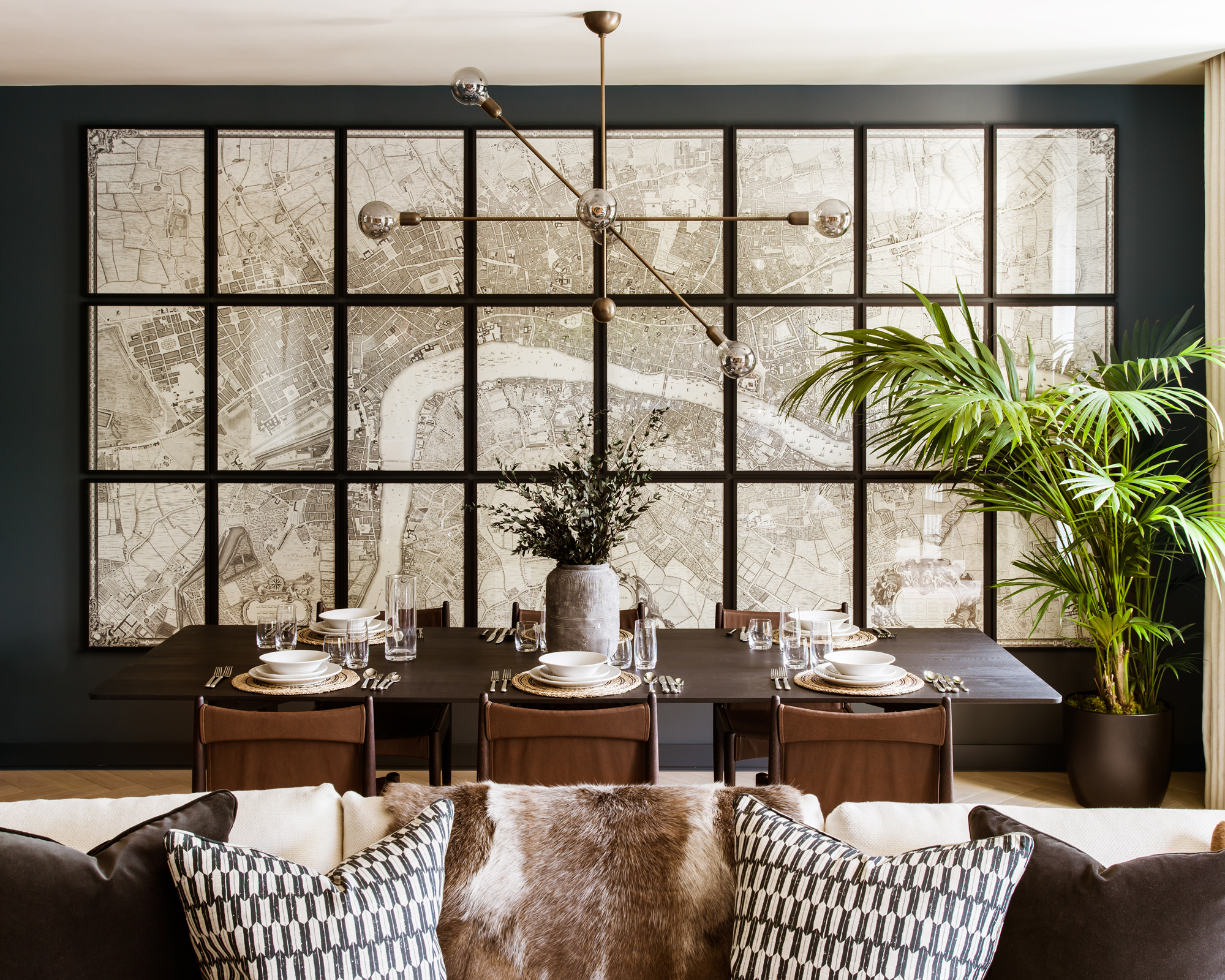 A dining room and living area with black walls and large map artwork across one wall, and wooden dining table and chairs