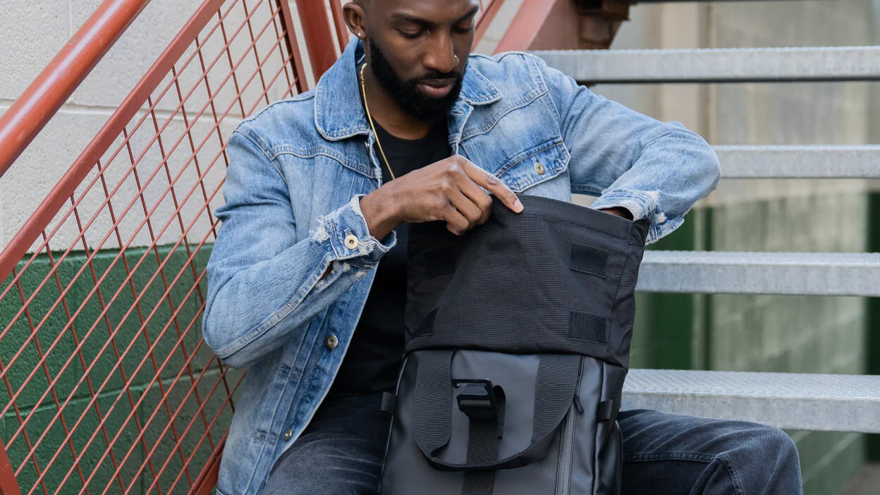 A person opens the roll top on the Wandrd Prvke camera backpack