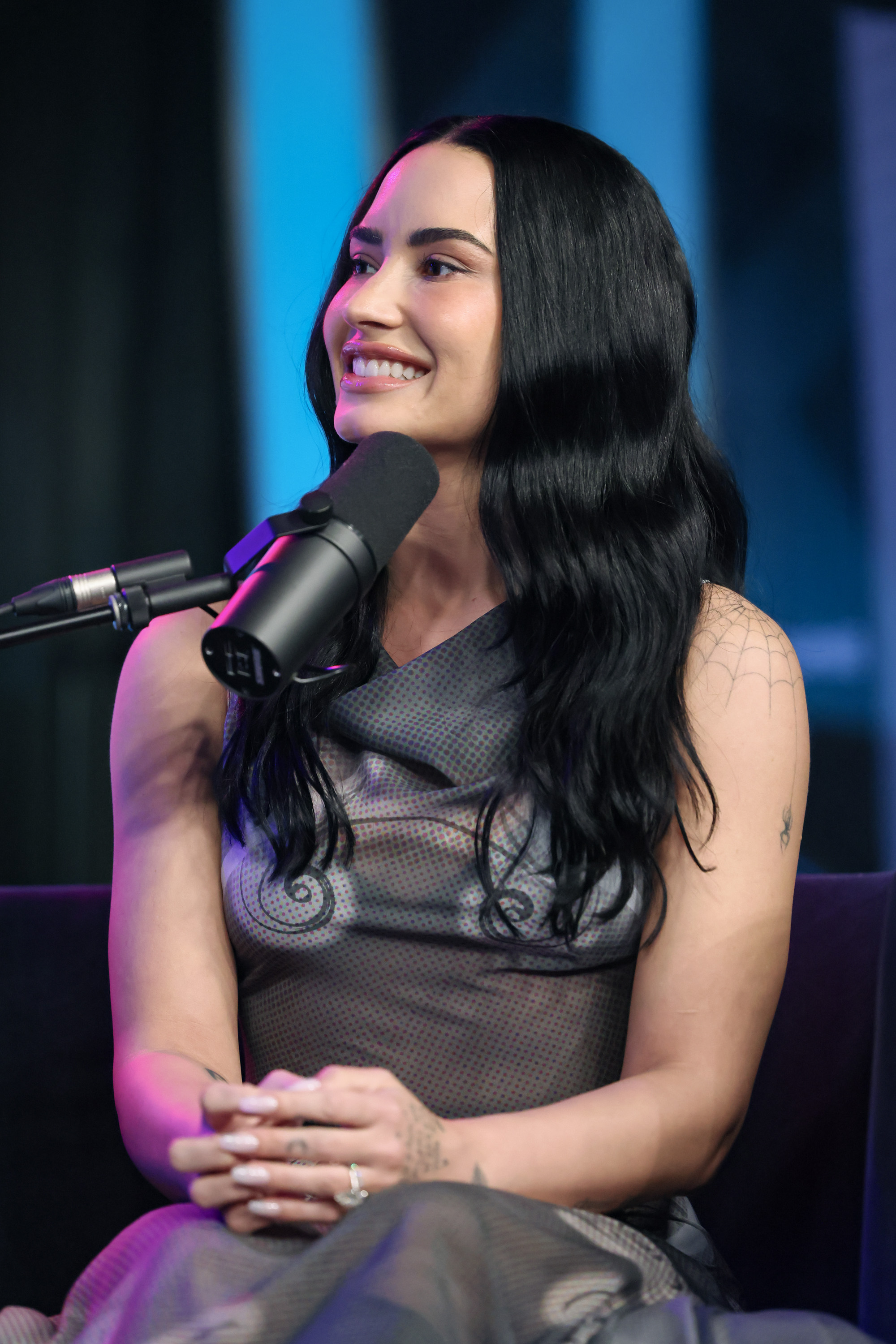 a white woman with long, dark hair wearing a sheer, gray dress while talking into microphone during a radio show