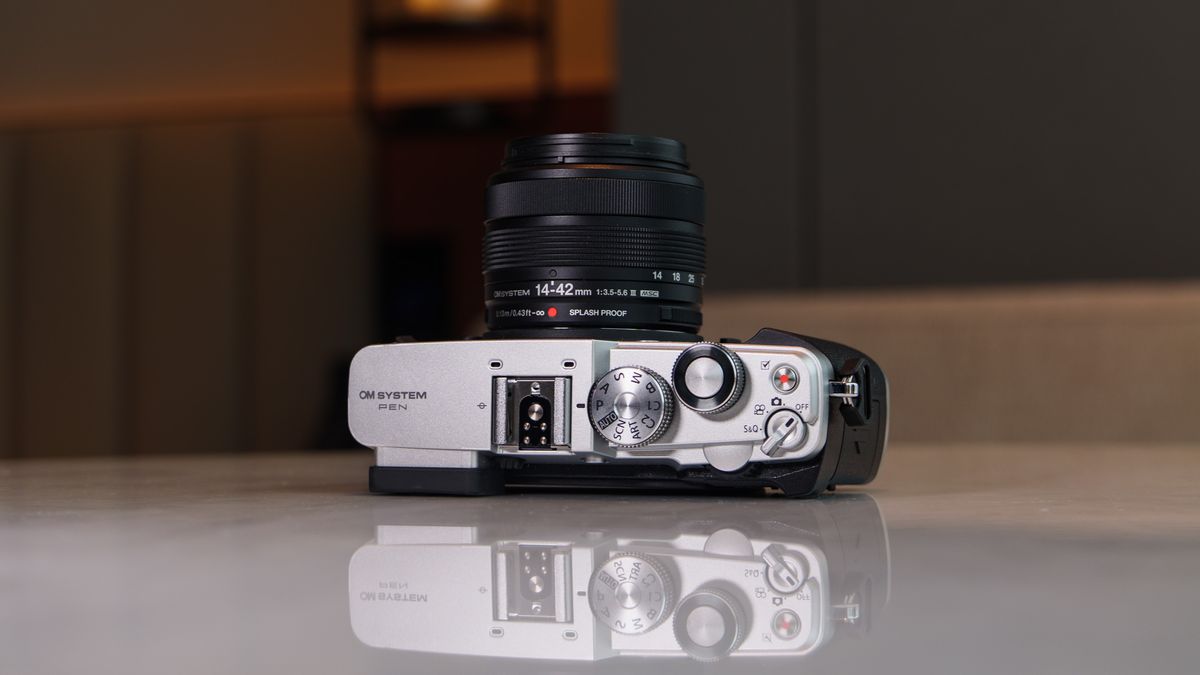 OM System PEN mirrorless camera on a white marble surface in a modern room with lantern in the background, it's on its back with the top plate in view