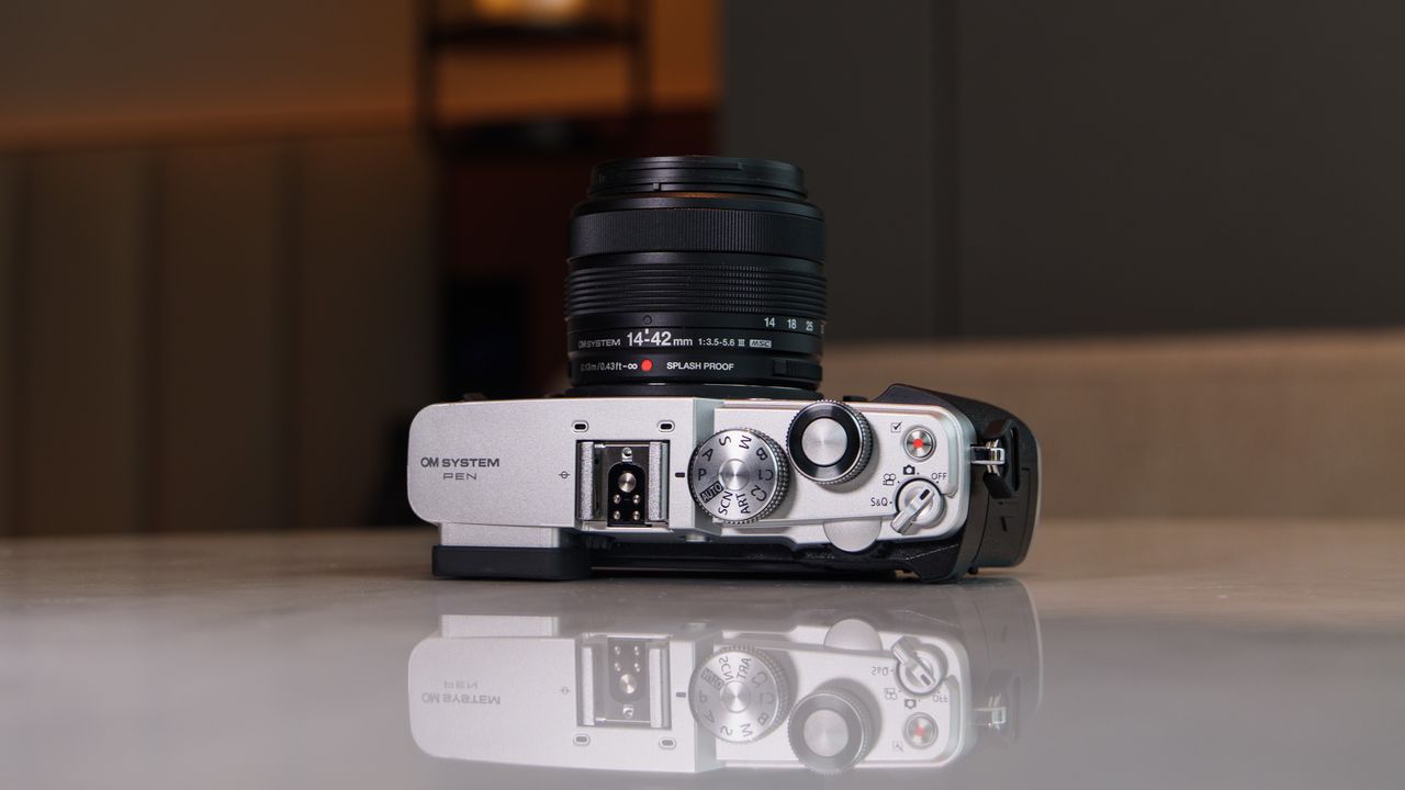 OM System PEN mirrorless camera on a white marble surface in a modern room with lantern in the background, it's on its back with the top plate in view