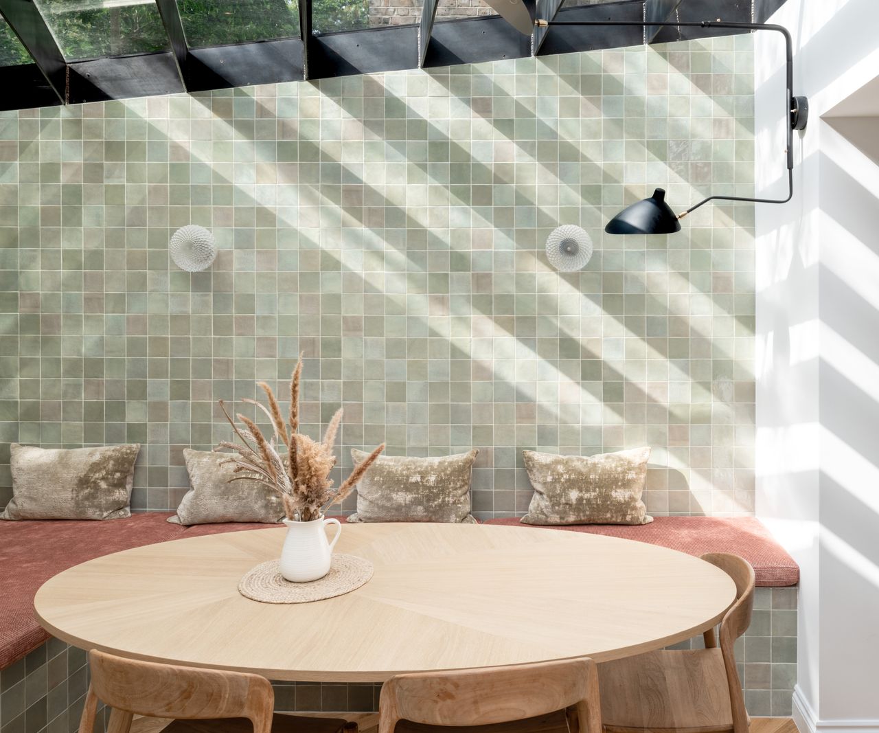 dining room with tiled walls, black and glass finned roof, banquette seating and round wooden table and chairs