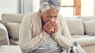 Woman sitting on a couch blowing her nose into a tissue