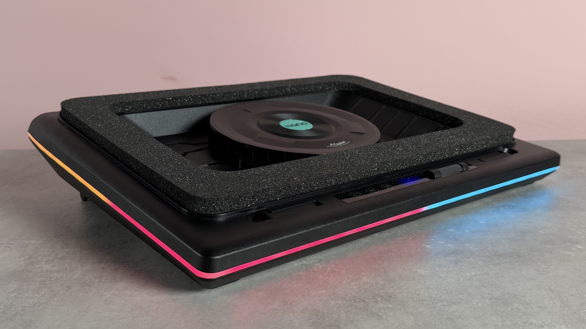 The Llano RGB Laptop Cooling Pad with RGB lighting enabled at a 3/4s angle in front of a pink background.