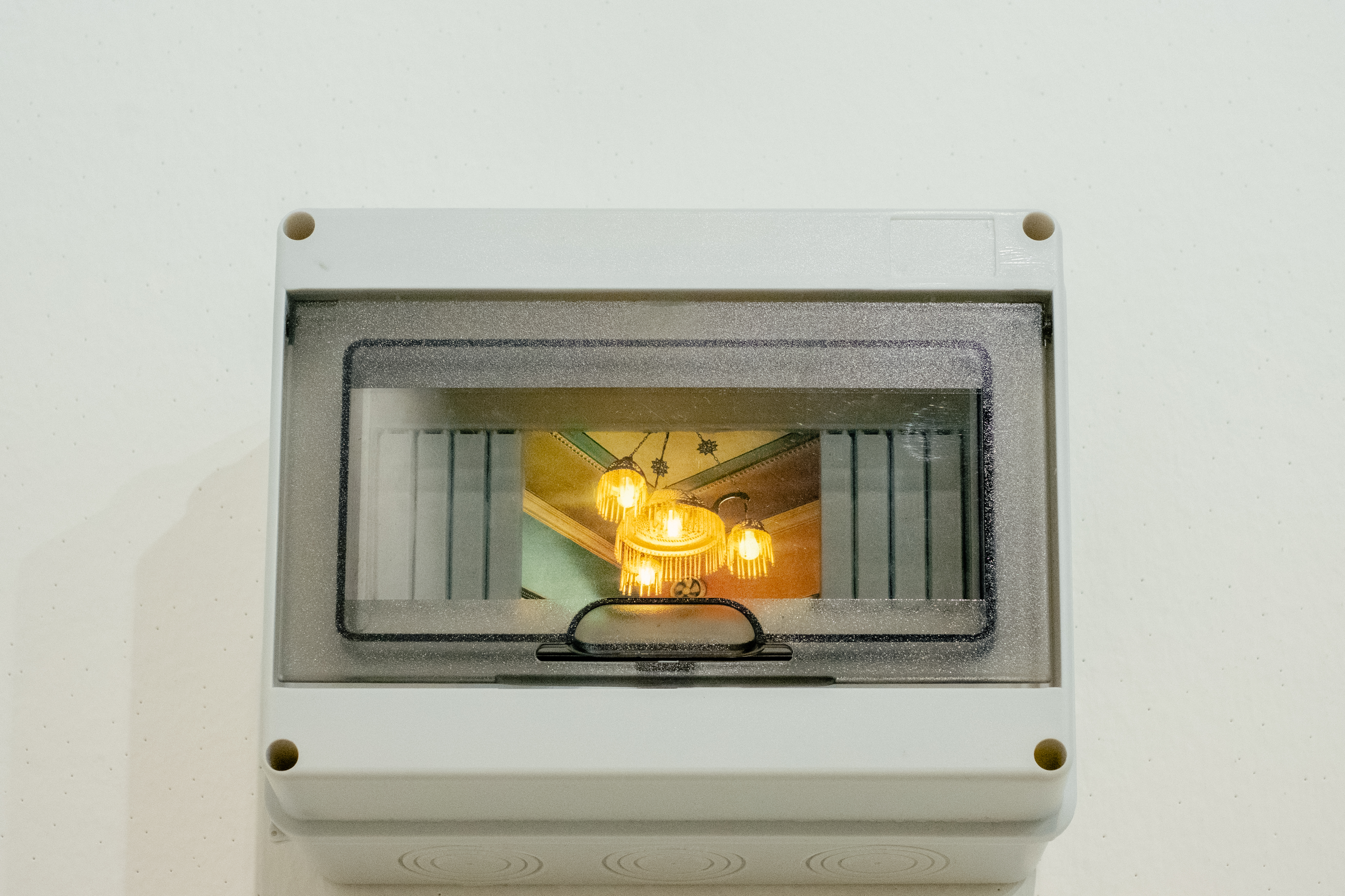 A chandelier glowing with warm light is captured in a photograph back-lit inside an electricity box as part of an art installation.