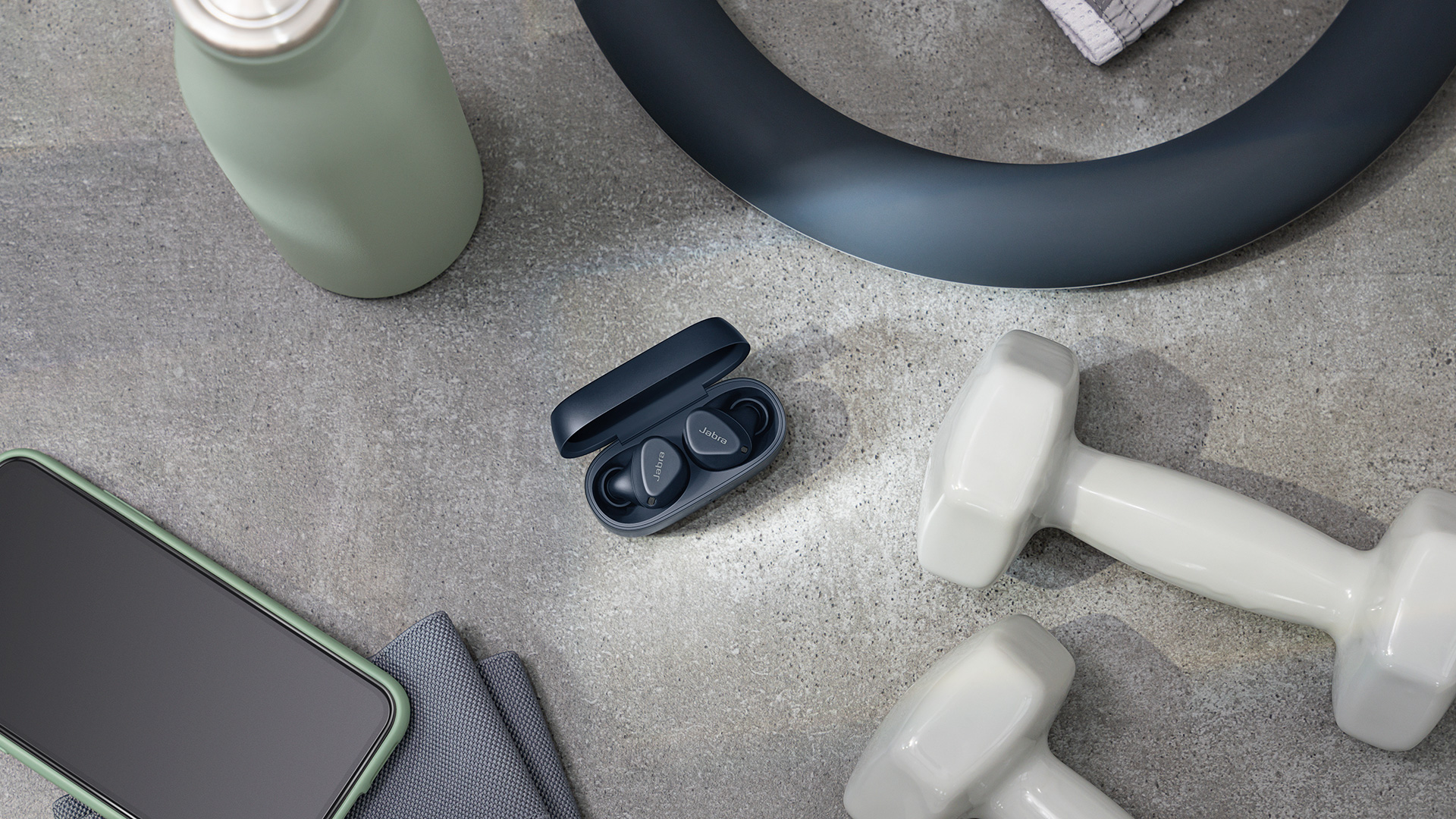Jabra Elite 4 Active in black in their charging case, surrounded by fitness equipment
