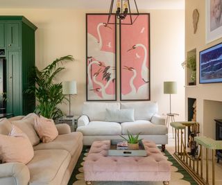 living room with light pink walls, pink ottoman and artwork, green kitchen cabinets in corner